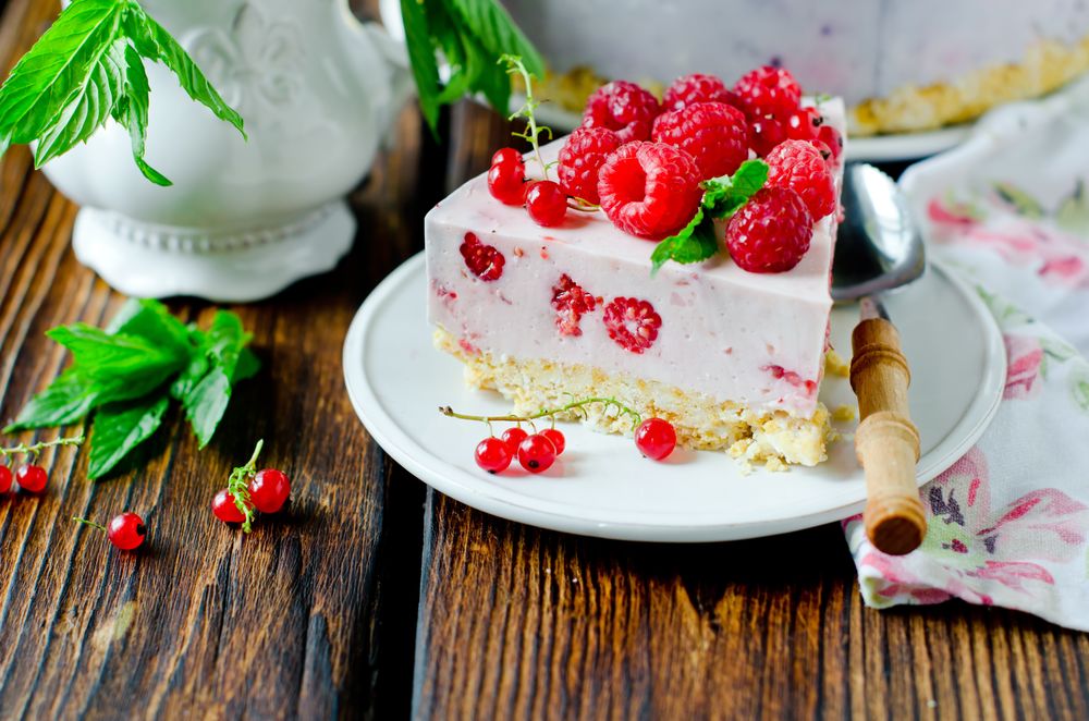 Обои для рабочего стола Кусочек кремового торта со свежими ягодами красной смородины и малины на блюдечке с ложкой