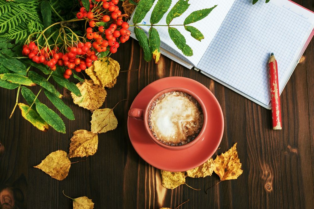 Обои для рабочего стола Осенний натюрморт на столе: чашка кофе, блокнот, карандаш, желтые листья и гроздь рябины