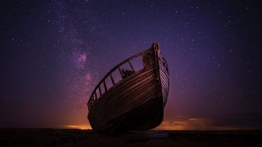 Обои для рабочего стола Разбитая лодка на берегу, на фоне красивого звездного неба
