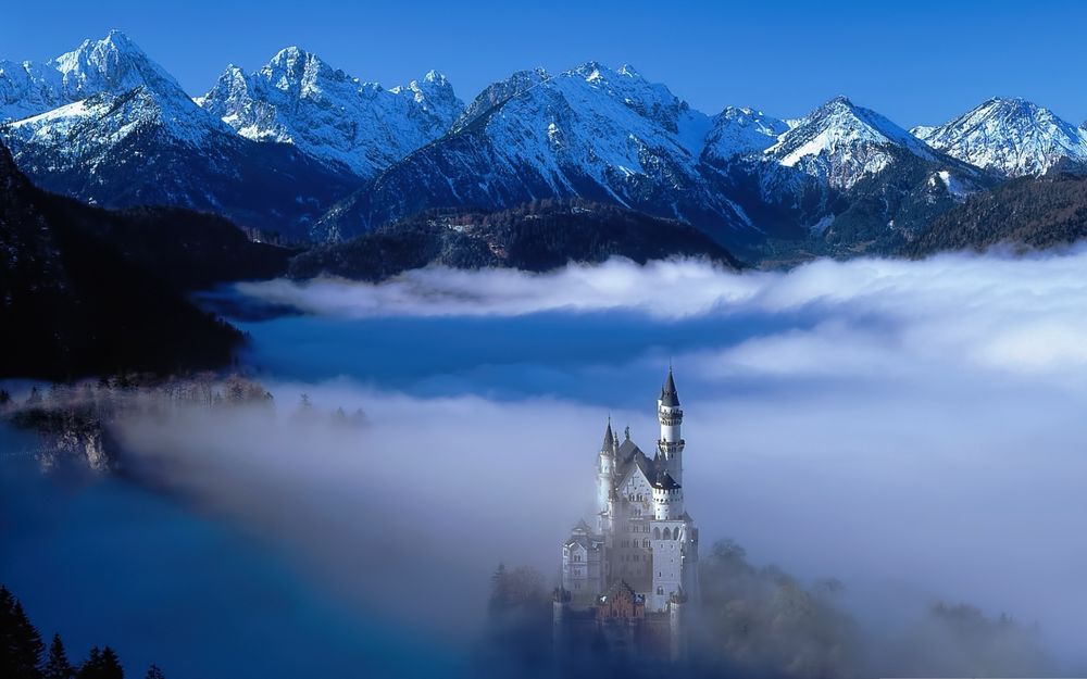 Обои для рабочего стола Замок Нойшванштайн, Германия в тумане на фоне снежных гор