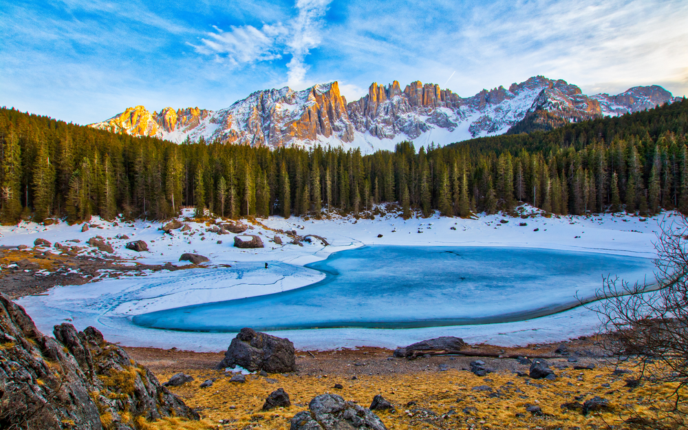 Обои для рабочего стола Небольшое замерзшее озеро Karersee / Карецца в Italy / Италии возле леса и заснеженных гор