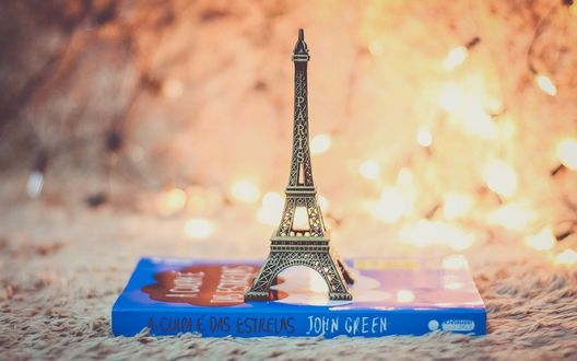 Обои на рабочий стол Фигурка Эйфелевой башни стоит на книге возле горящей гирлянды