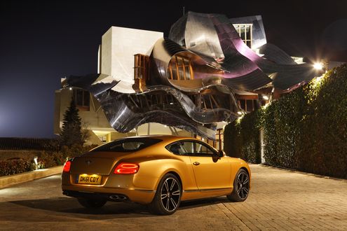 Обои на рабочий стол Золотистый Bentley Continental / Бентли Континенталь стоит у дома с необычным дизайном