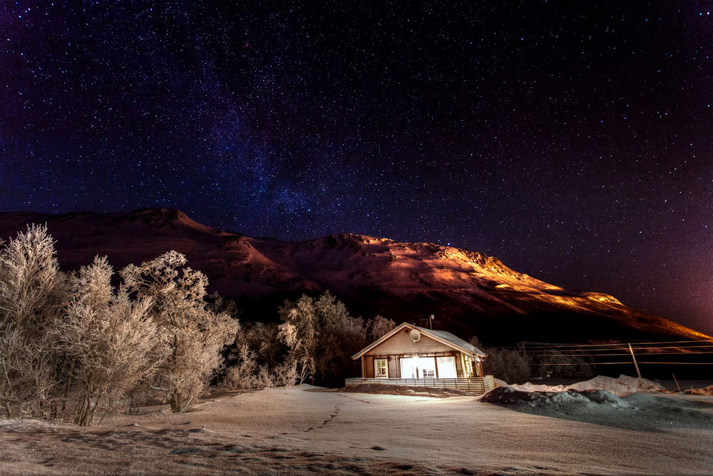 Обои для рабочего стола Одинокий домик ночью на фоне зимней природы, гор и звездного неба