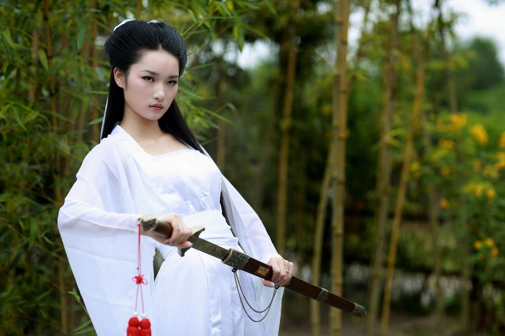 Обои для рабочего стола Красивая девушка в белом кимоно, с мечом в руках стоит на фоне природы