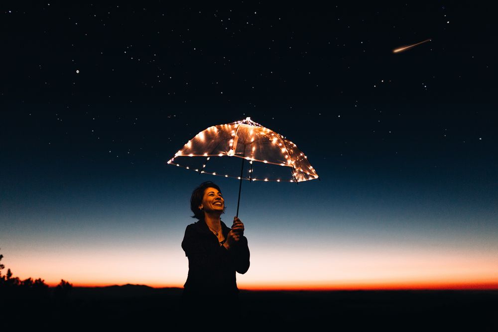 Обои для рабочего стола Девушка с сияющим зонтом стоит на фоне ночного неба