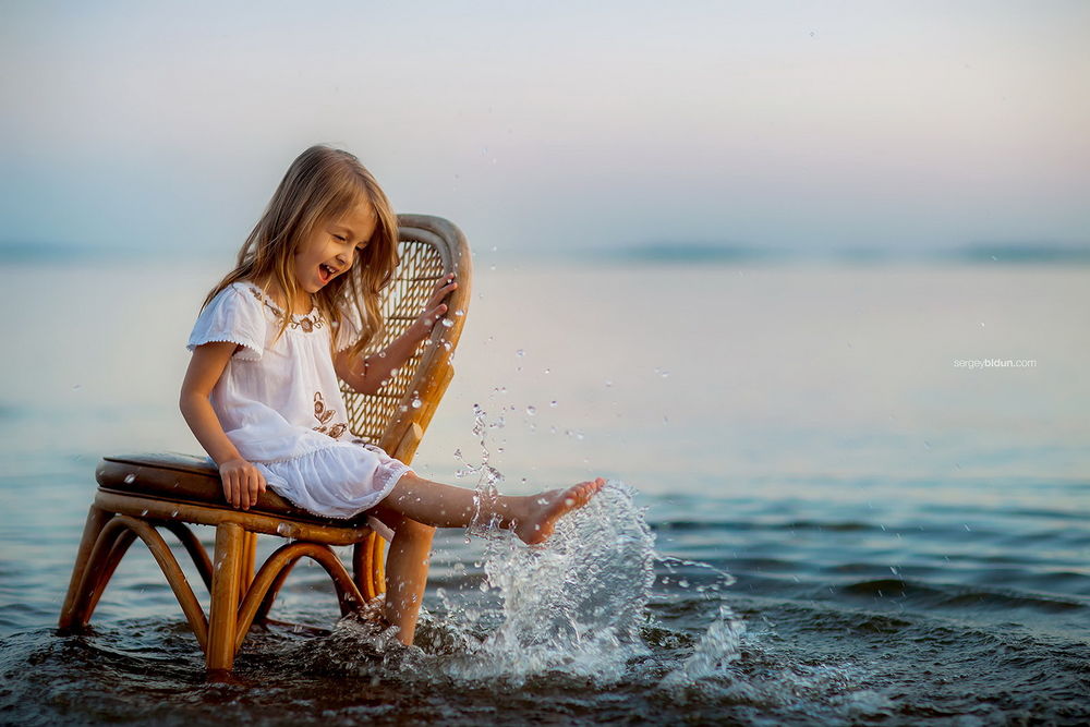 Обои для рабочего стола Радостная девочка сидит на стуле, болтая ножками в воде, фотограф Sergey Bidun