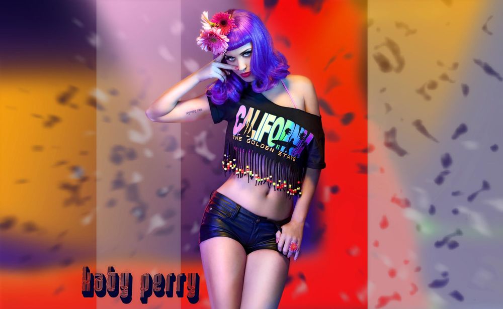 Обои для рабочего стола Певица Katy Perry / Кети Перри позирует, стоя с цветами в волосах и в футболке с надписью: California the golden state / Калифорния золотой штат, на фоне боке
