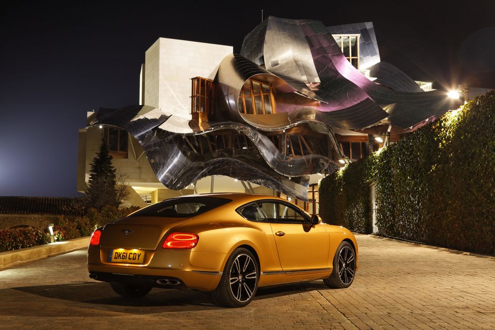 Обои для рабочего стола Золотистый Bentley Continental / Бентли Континенталь стоит у дома с необычным дизайном