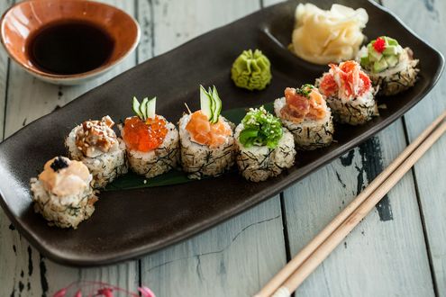 Обои на рабочий стол Японская кухня: ассорти из рисовых роллов с рыбой, икрой и огурцом, рядом соус, маринованный имбирь, васаби и палочки для еды