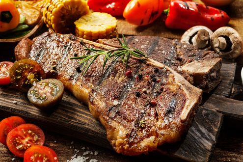 Обои на рабочий стол Запеченное мясо рядом с грибами, паприкой, кукурузой и помидорами лежит на доске