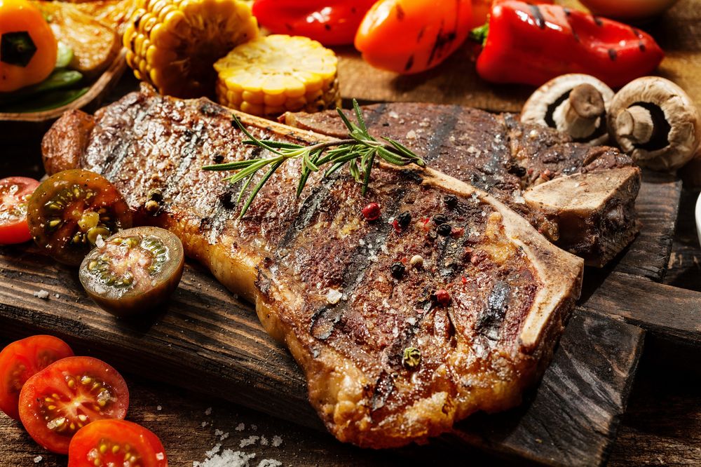 Обои для рабочего стола Запеченное мясо рядом с грибами, паприкой, кукурузой и помидорами лежит на доске
