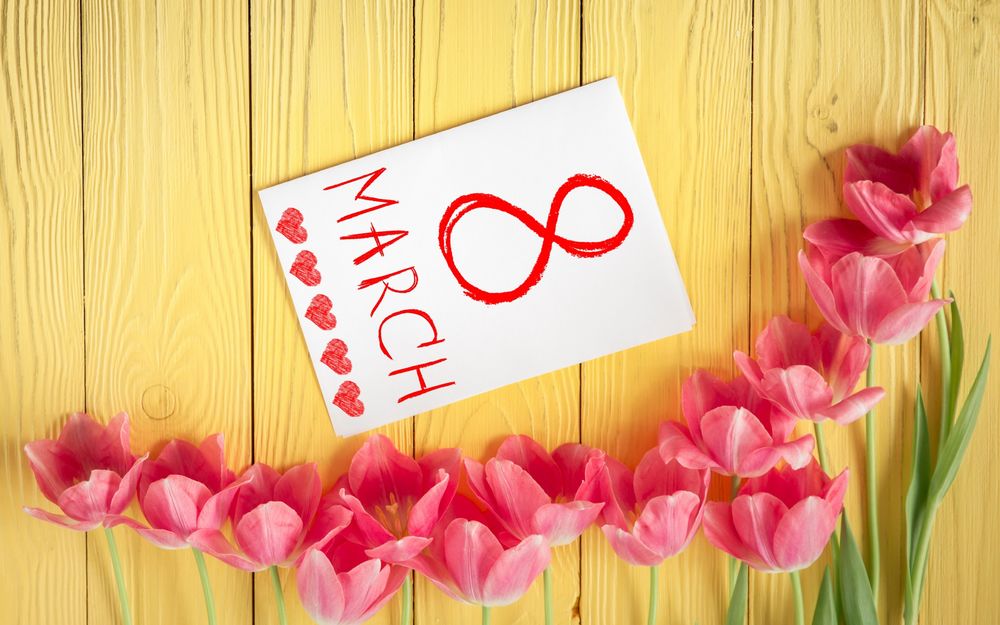 Обои для рабочего стола Розовые тюльпаны лежат рядом с открыткой, на которой нарисованы сердечки и написано 8 march / 8 марта