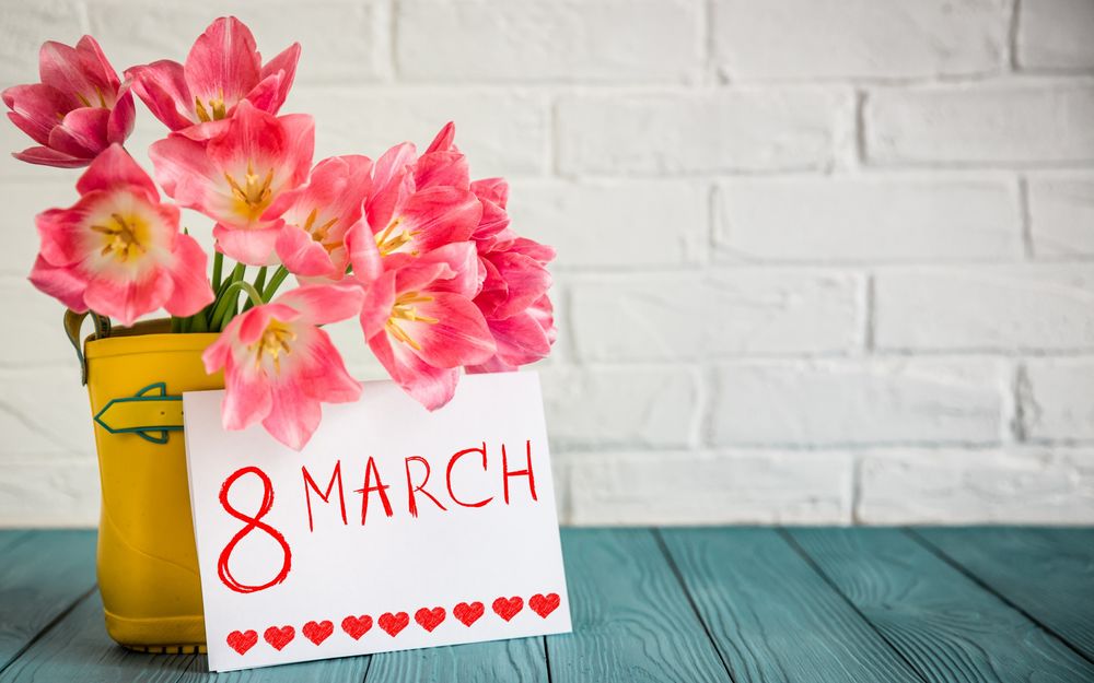 Обои для рабочего стола Розовые тюльпаны в желтом резиновом сапоге и открытка с текстом 8 March / 8 Марта с сердечками на фоне кирпичной стены