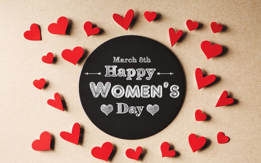Обои для рабочего стола Сердечки лежат вокруг черной дощечки с фразой 8 March, Happy Womans Day / 8 марта, Международный женский день на ней