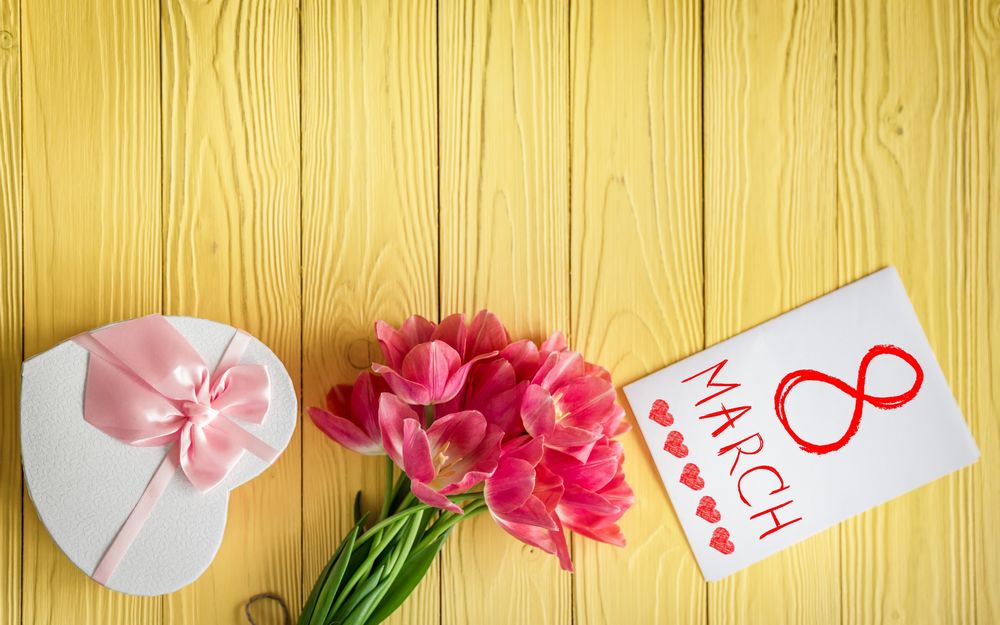 Обои для рабочего стола Букет розовых тюльпанов лежит рядом с подарком в форме сердца и открыткой, на которой написано 8 march / 8 марта и нарисованы сердечки на желтом фоне