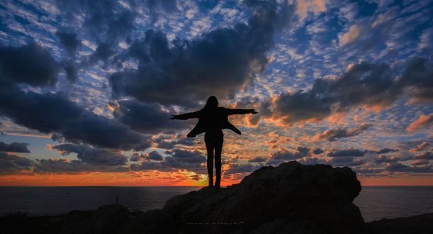 Обои на рабочий стол Девушка стоит на камне, на фоне облачного неба, фотограф sherin atrouni