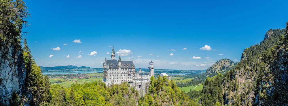 Обои для рабочего стола Замок Нойшванштайн, Бавария / Schloss Neuschwanstein, Bavaria на фоне синего неба с редкими облаками в обрамлении гор, by Karlheinz Melzer