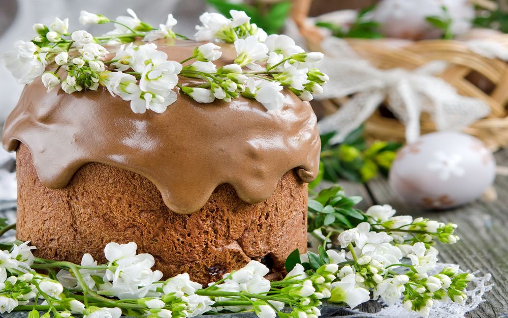 Обои для рабочего стола Пасхальный кулич, покрытый шоколадной глазурью и украшенный живыми цветами, лежит на столе