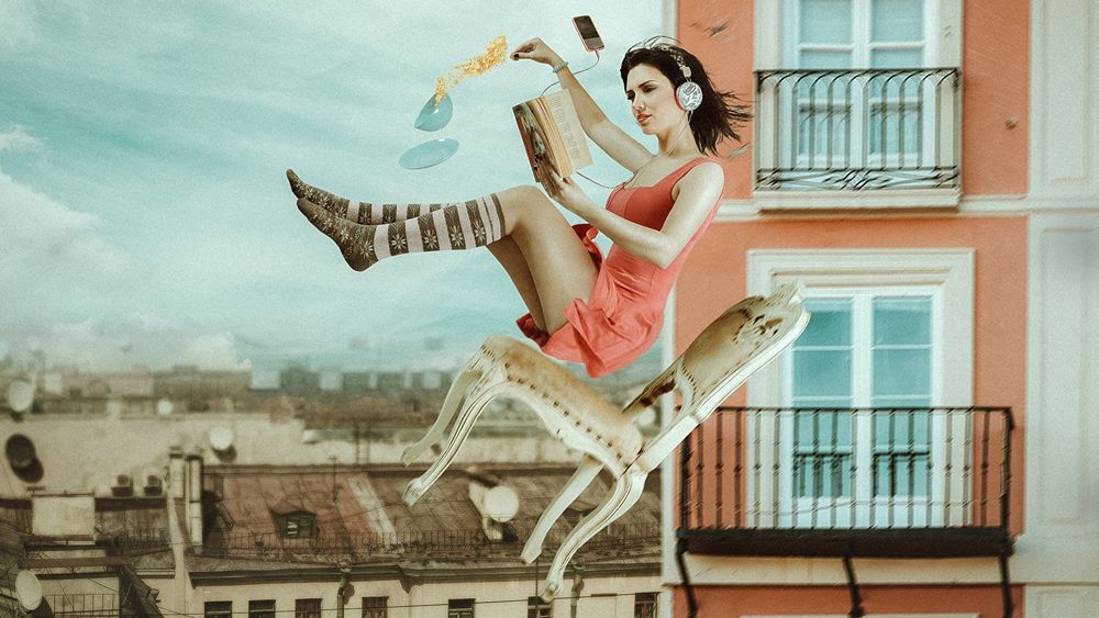 Обои для рабочего стола Девушка в наушниках и с книгой парит в воздухе над крышами домов