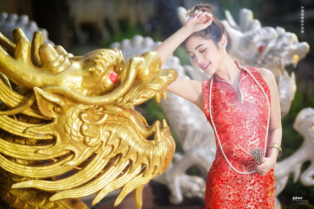 Обои для рабочего стола Азиатка китаянка в красном платье стоит закрыв глаза рядом с позолоченной головой дракона