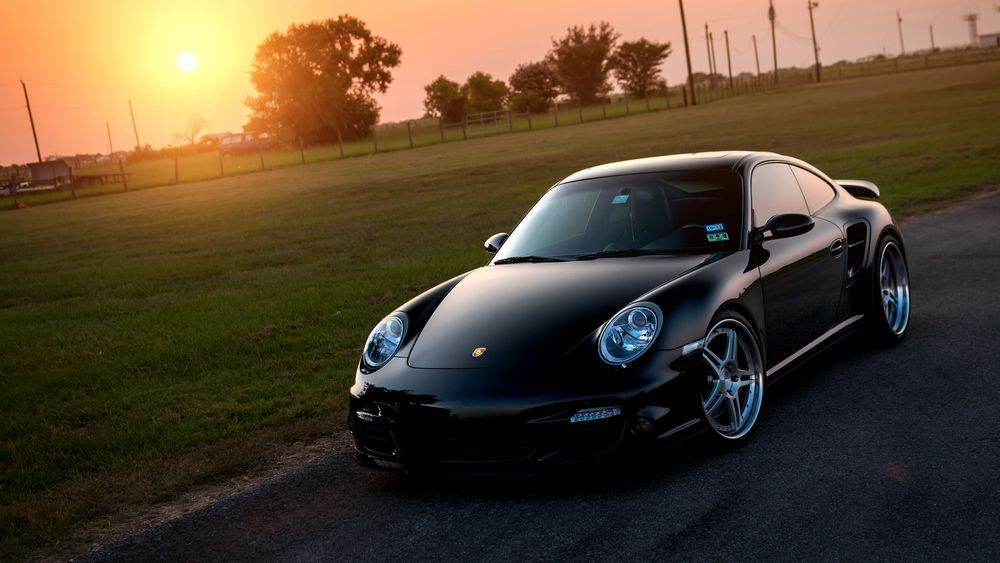 Обои для рабочего стола Porsche 911 стоит на дороге на фоне солнца
