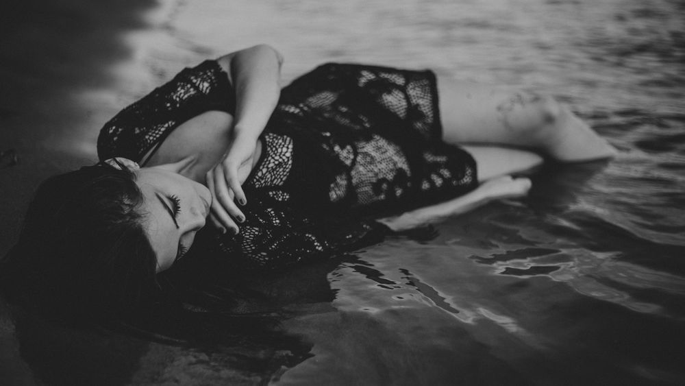 Обои для рабочего стола Девушка в черном платье лежит на берегу, опустив ноги в воду, by StockSnap