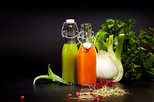 Обои на рабочий стол Две бутылки с соками, рядом лук-порей, петрушка, алоэ и зерна граната