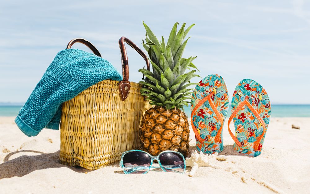 Обои для рабочего стола Соломенная сумка с синим покрывалом, ананас, тапки и очки лежат на пляже и напоминают, что скоро отпуск