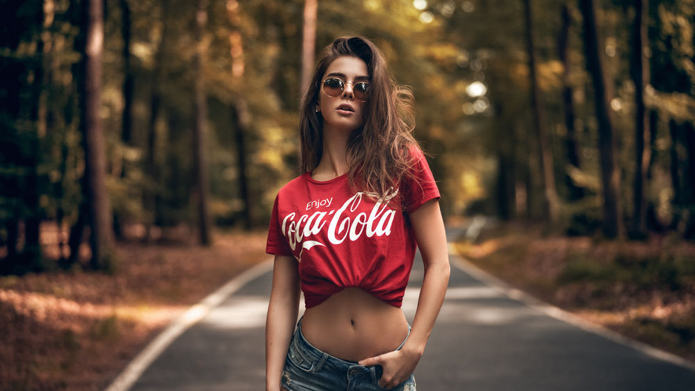 Обои для рабочего стола Модель Sara Tessitore в очках и футболке с надписью coca-cola стоит на дороге. Фотограф Martin Kuhn