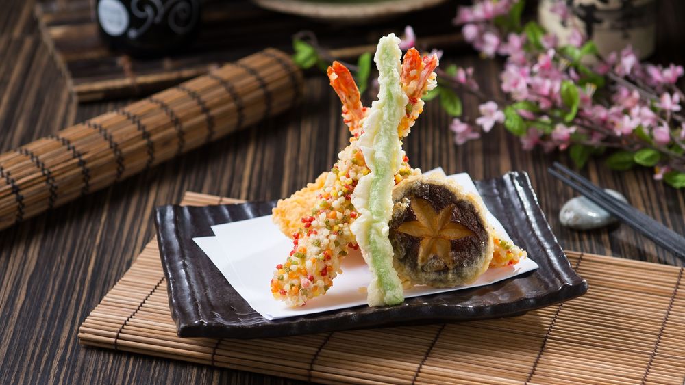 Обои для рабочего стола Японская кухня: блюдо с креветками в кляре на циновке, рядом палочки для еды и цветы