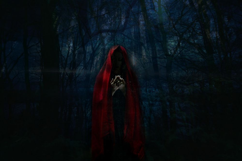 Обои для рабочего стола Женщина в красном плаще, закрывающем фигуру на фоне мрачного черного леса