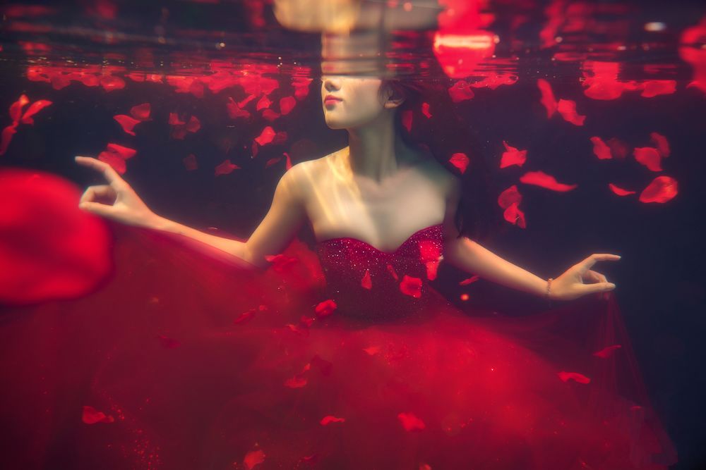 Обои для рабочего стола Азиатка в красном платье с корсетом плавает в воде среди красных лепестков