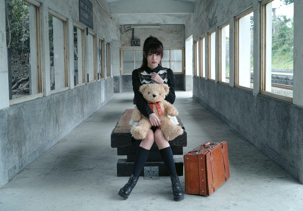 Обои для рабочего стола Девушка азиатской внешности с игрушечным мишкой сидит рядом с чемоданом