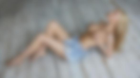 Обои для рабочего стола Стройная блондинка Екатерина Чернышева в приспущенном джинсовом комбинезоне позирует, лежа на полу помещения, прикрывая руками грудь. Фотограф Дмитрий Лобанов