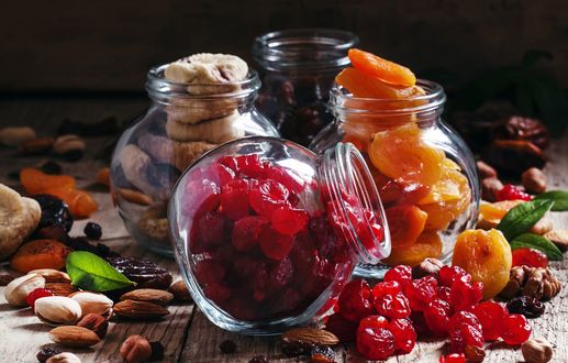 Обои на рабочий стол Четыре баночки с курагой, инжиром, черносливом и сушеной вишней среди россыпи орехов, изюма и других сухофруктов