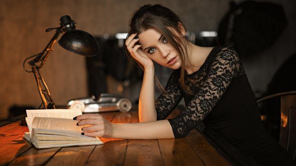 Обои на рабочий стол Модель Ksenia Kokoreva / Ксения Кокорева в черном платье позирует, сидя за столом с книгой. Фотограф Сергей Фат