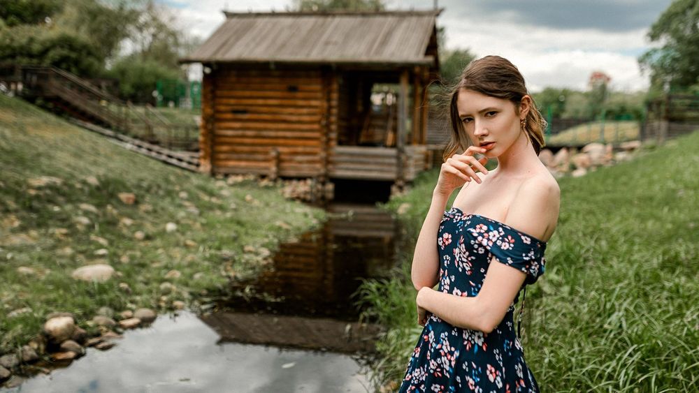 Обои для рабочего стола Модель Disha Shemetova / Диша Шеметова в платье с открытыми плечами позирует, стоя на берегу небольшой речки. Фотограф Евгений Маркалев