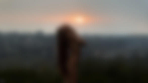 Обои для рабочего стола Обнаженная девушка с длинными волосами стоит на фоне заката над городом. Фотограф Tomash