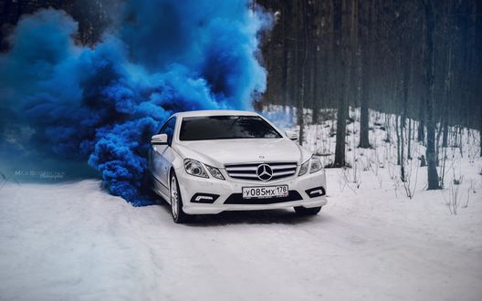 Обои на рабочий стол Белый Mercedes E250 (C207) едет по зимней дороге с синим дымом