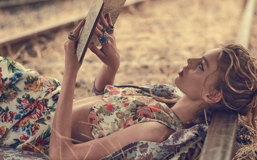 Обои для рабочего стола Девушка с книгой в руках лежит на земле между рельсами
