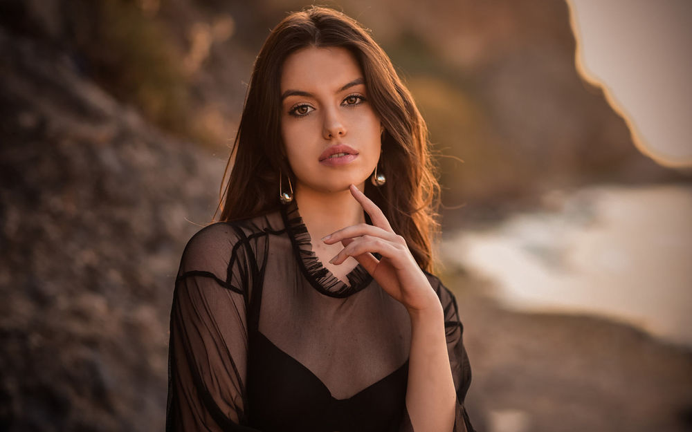 Обои для рабочего стола Модель DiLara Kirmit стоит на фоне моря вдалеке от нее и держит руку у лица, фотограф Нуреттин Йылдырым