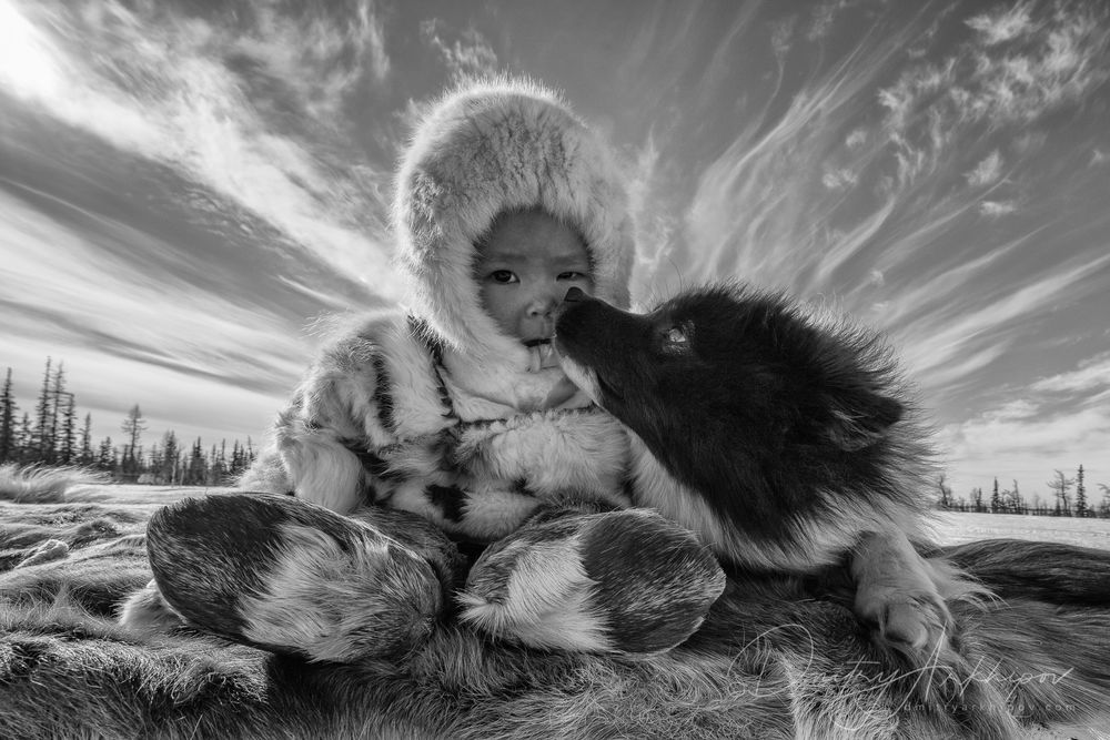 Обои для рабочего стола Мальчик в меховой одежде и собака отдыхают на траве, фотограф Дмитрий Архипов