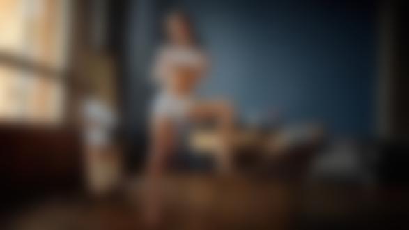 Обои для рабочего стола Модель Екатерина Зуева в приподнятой кофточке и шортах позирует, стоя в комнате, поставив ногу на плетеное кресло. Фотограф Георгий Чернядьев