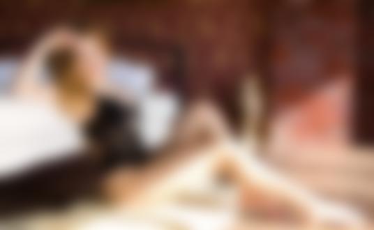 Обои для рабочего стола Симпатичная девушка в черном кружевном нижнем белье позирует, сидя на полу комнаты у кровати, на фоне кирпичной стены. Фотограф Григорий Лифин