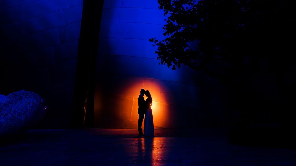 Обои для рабочего стола Силуэты пары влюбленных в ночи, освещаемых красным светом на фоне стены здания