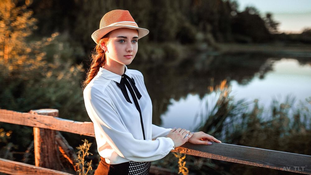 Обои для рабочего стола Девушка Настя в шляпе и в белой рубашке позирует, стоя у ограждения моста на размытом фоне водоема и природы. Фотограф Aleksandr Suhar