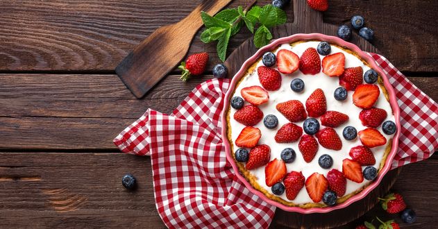 Обои на рабочий стол Вкусный пирог - сметанник, украшенный клубникой и черникой, стоит на клетчатом красном полотенце