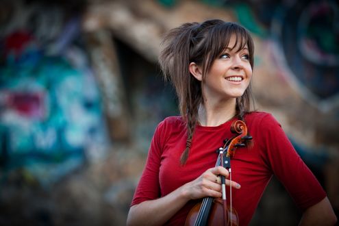 Обои на рабочий стол Скрипачка Lindsey Stirling / Лииндси Стиирлинг в красном стоит со скрипкой в руках