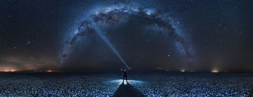 Обои для рабочего стола Мужчина стоит ночью в цветущем поле и светит фонарем в небо на фоне млечного пути, фотограф Gonzalo Javier Santile